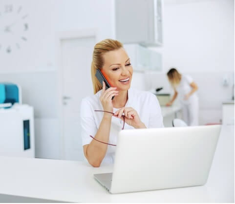 Dentista no telefone celular e com um computador na frente