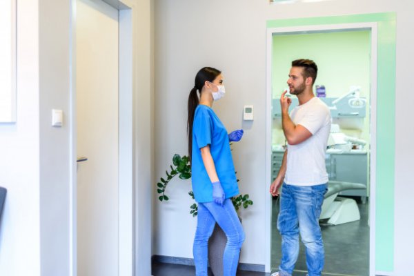 Uma mulher conversando com um homem que está com a mão sinalizando dor no dente