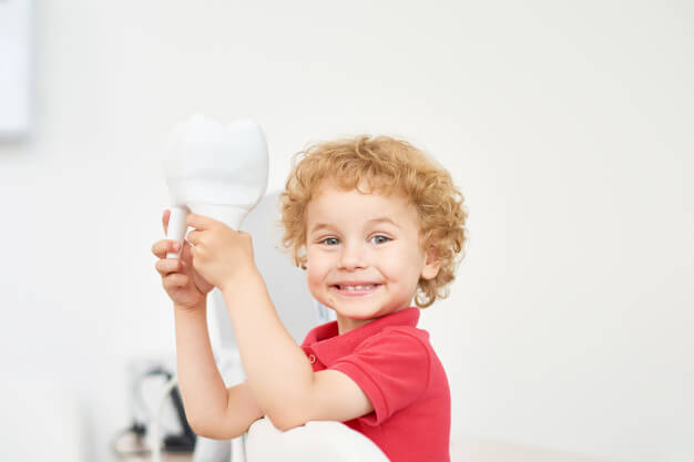 Criança sorrindo em consultório segurando o dente