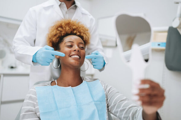 Paciente sorridente avalia o resultado do atendimento odontológico no espelho, representando a importância da experiência do paciente