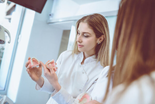 Dentista segura modelos de arcada dentária durante explicação sobre kits de odontologia indispensáveis