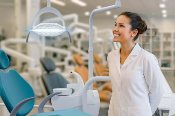 Dentista sorridente em consultório moderno observando o equipamento de iluminação ao lado da melhor cadeira odontológica, destacando conforto e tecnologia