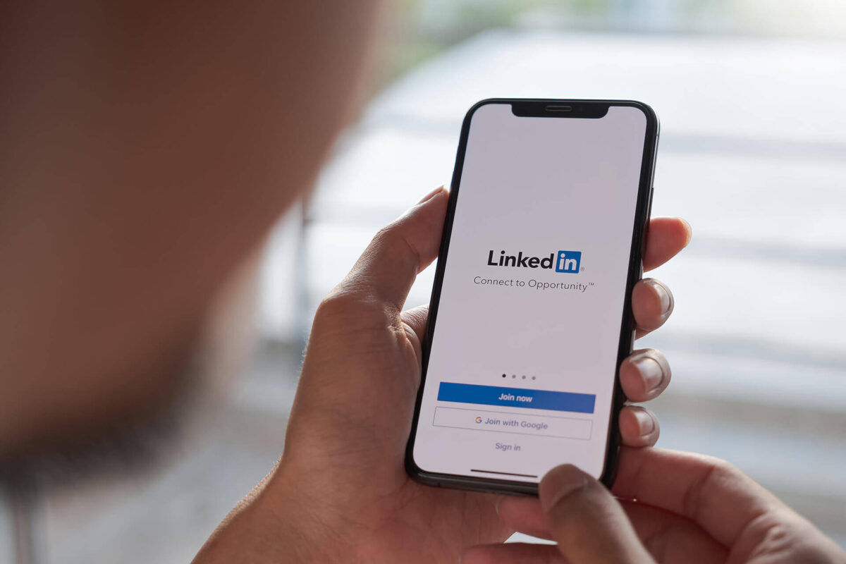 Linkedin para dentistas: aumente as visitas no seu perfil com isso gerente de consultório odontológico Pessoa acessando o aplicativo do LinkedIn no celular, representando a presença digital estratégica no LinkedIn para dentistas que buscam aumentar a visibilidade e oportunidades na carreira.