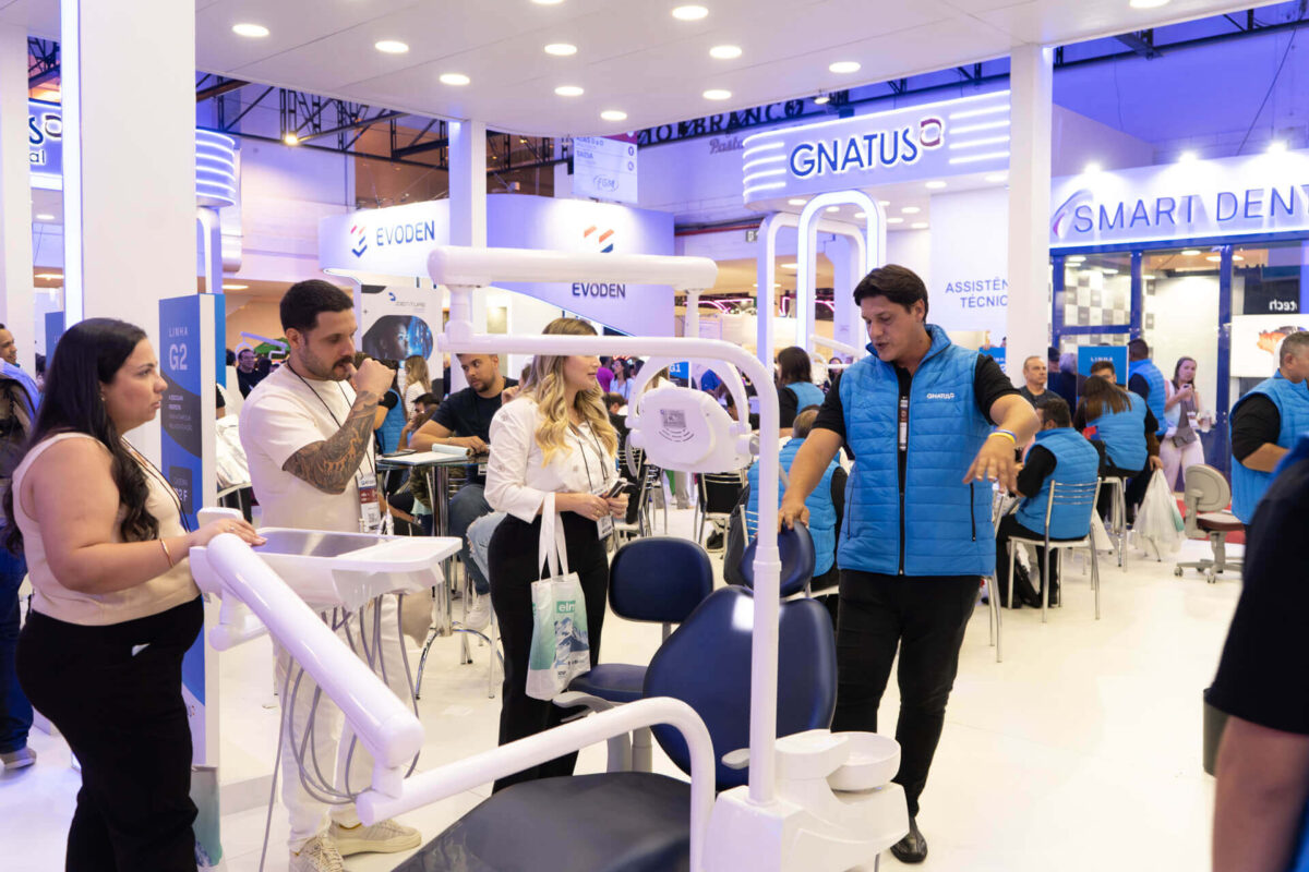 Profissionais analisando equipamentos odontológicos da Gnatus em feira do setor, com demonstração técnica ao vivo no estande.