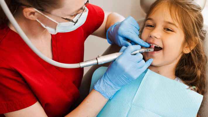 Dentista realizando atendimento odontológico infantil enquanto uma criança sorri durante a limpeza dos dentes