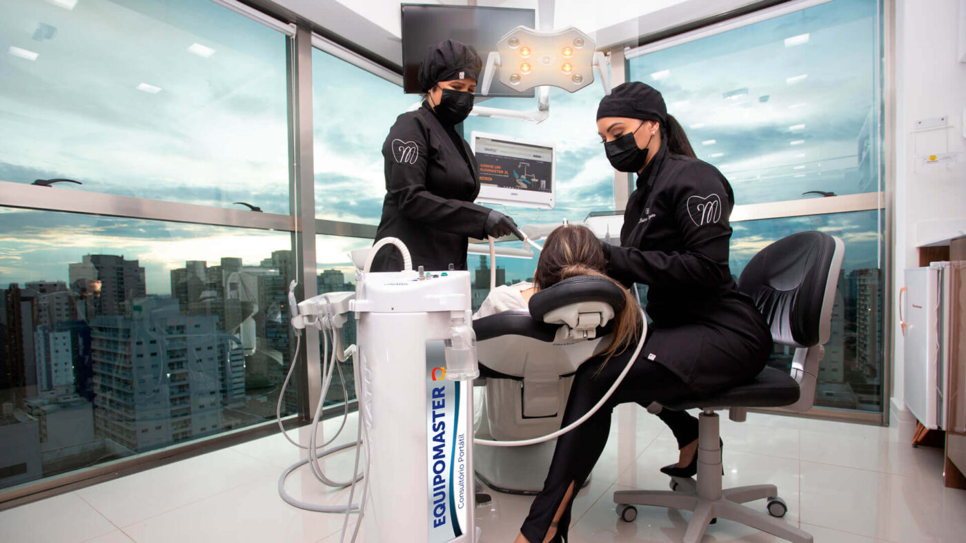 Profissionais atendendo paciente em clínica odontológica moderna com equipamentos de última geração e vista panorâmica da cidade.