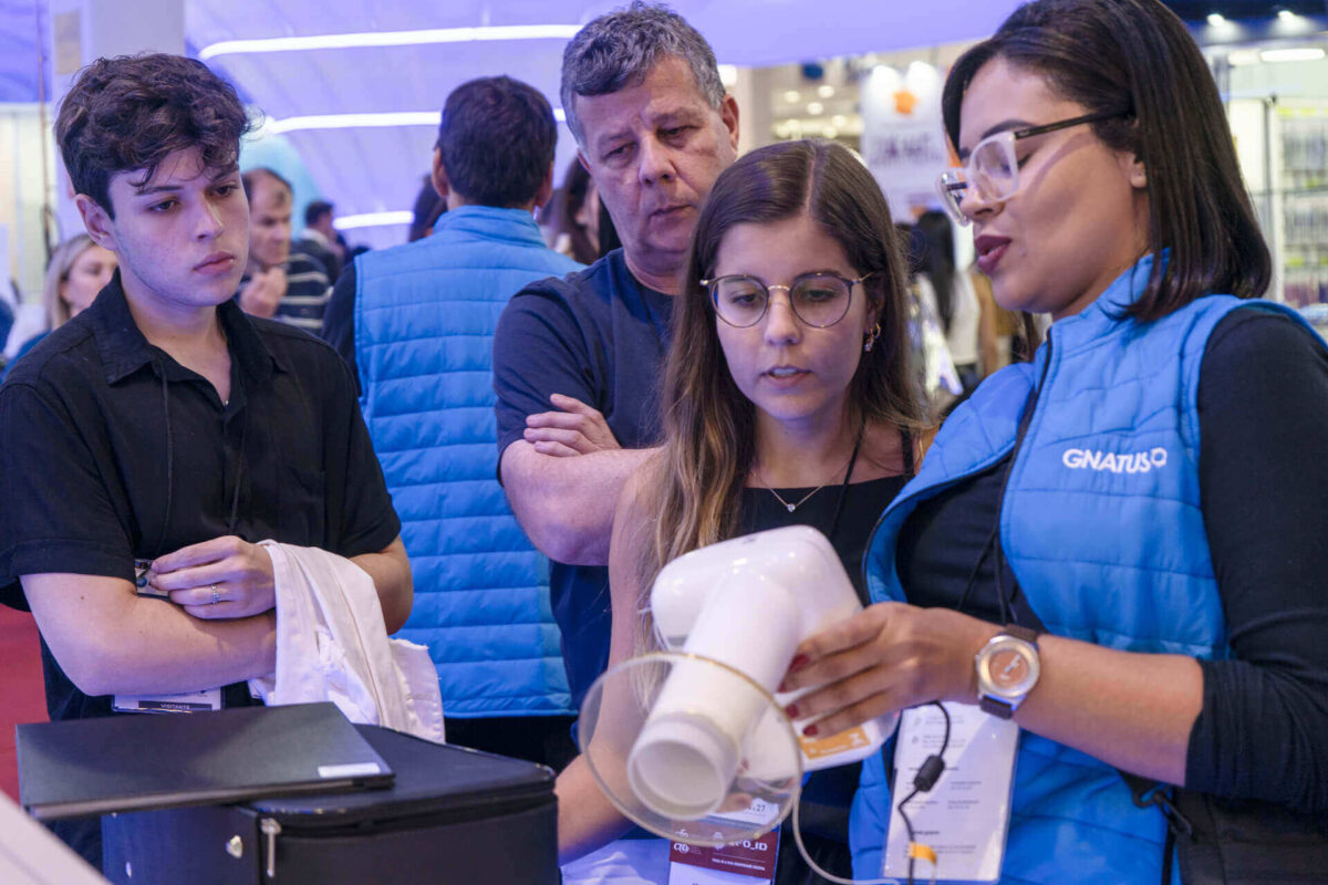 Profissionais observam demonstração técnica de um equipamento odontológico durante evento da área da saúde.