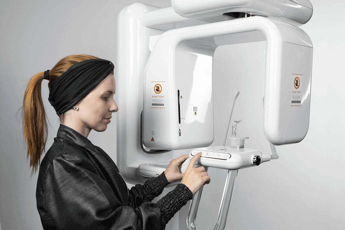 Vale a pena investir em um raio x panorâmico? Equipamento pode ser o diferencial da sua clínica raio x panorâmico Profissional posicionando paciente em exame com raio x panorâmico em clínica odontológica