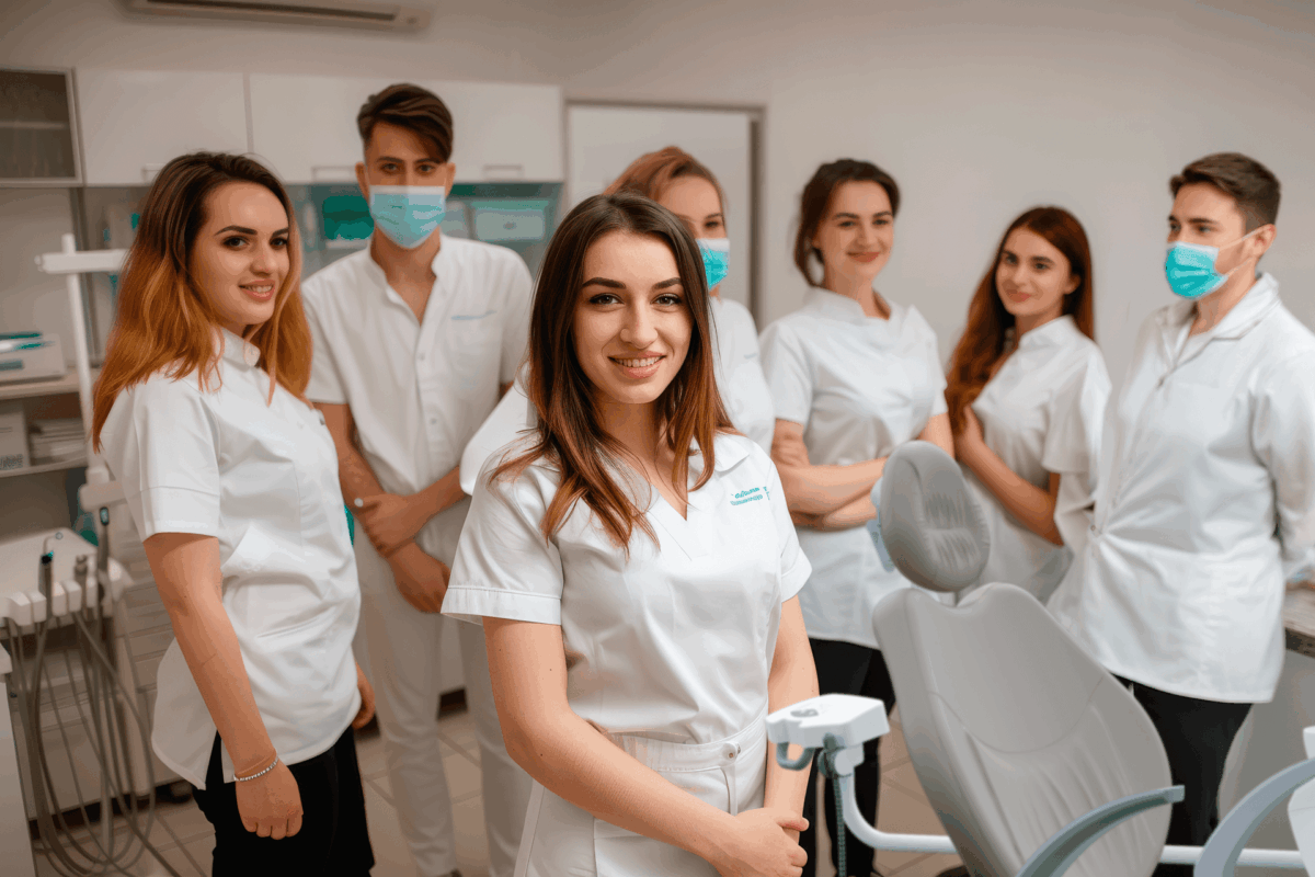 Estudantes e profissionais do curso de odontologia reunidos em clínica odontológica ao lado de cadeira de atendimento e equipamentos dentários.