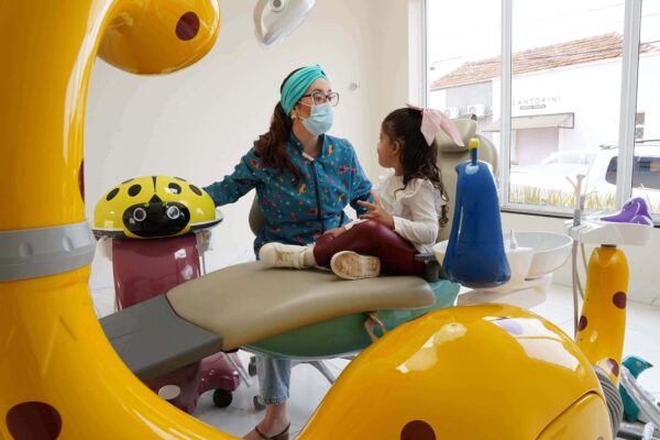 Criança em consulta odontológica interagindo com dentista em ambiente lúdico para reduzir o medo de dentista infantil.