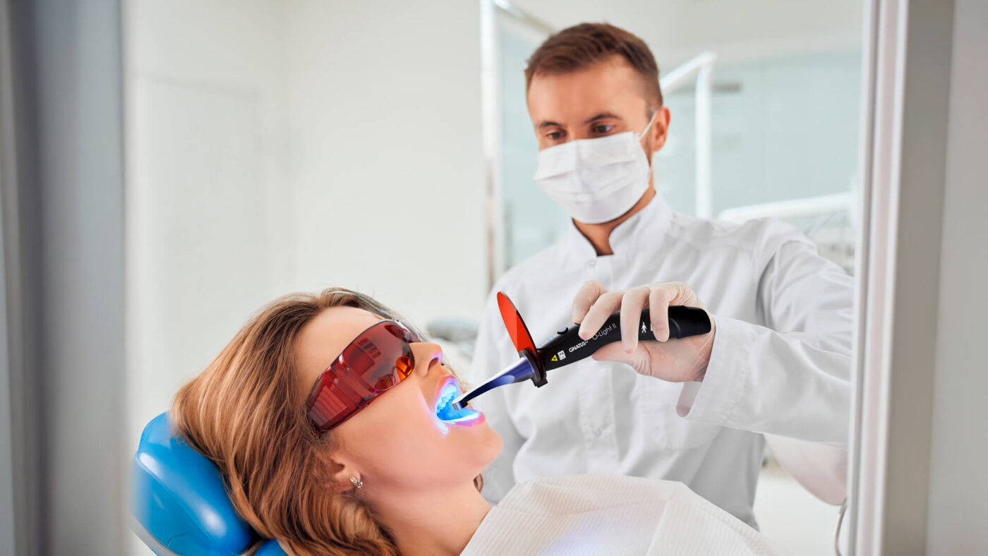 Dentista utilizando kit de restauração odontológica com fotopolimerizador em paciente durante procedimento clínico