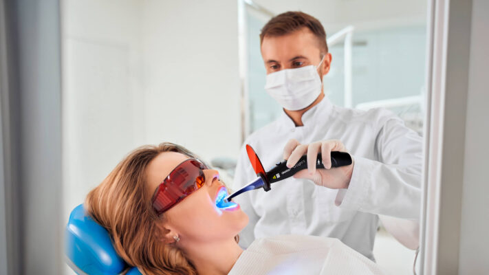 Dentista utilizando kit de restauração odontológica com fotopolimerizador em paciente durante procedimento clínico