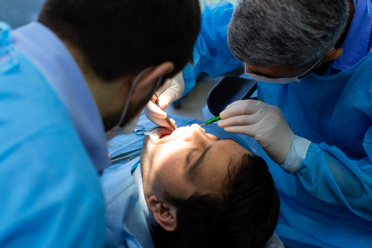 cirurgia odontologica Cirurgia odontológica realizada por dentistas com instrumentos cirúrgicos e equipamentos de proteção em ambiente clínico.