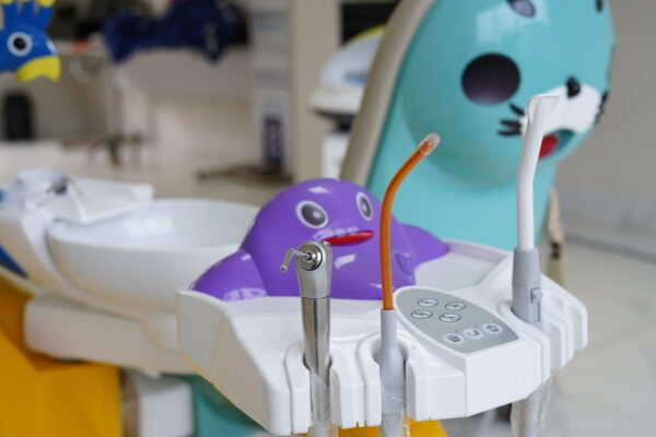 Equipamentos para odontopediatria com instrumentos odontológicos, painel de controle e cadeira infantil colorida em consultório adaptado para crianças.